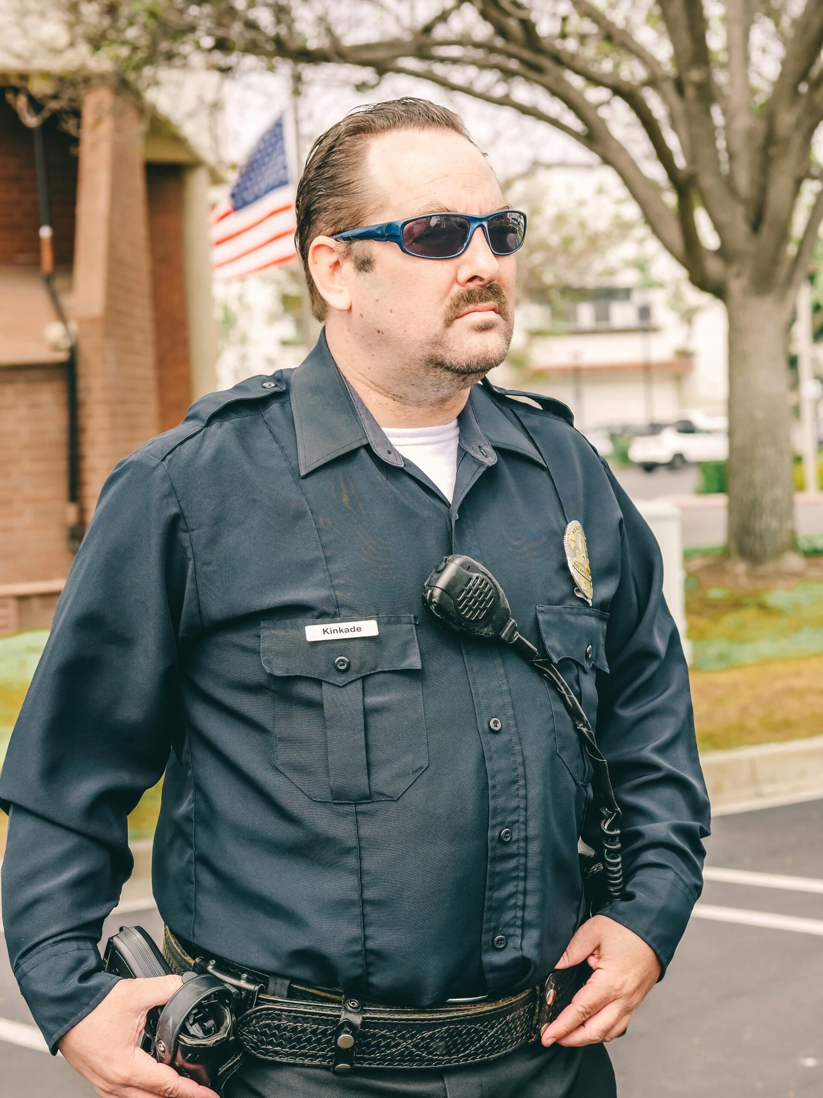 A police officer standing confidently in uniform with sunglasses, outdoors and on duty.