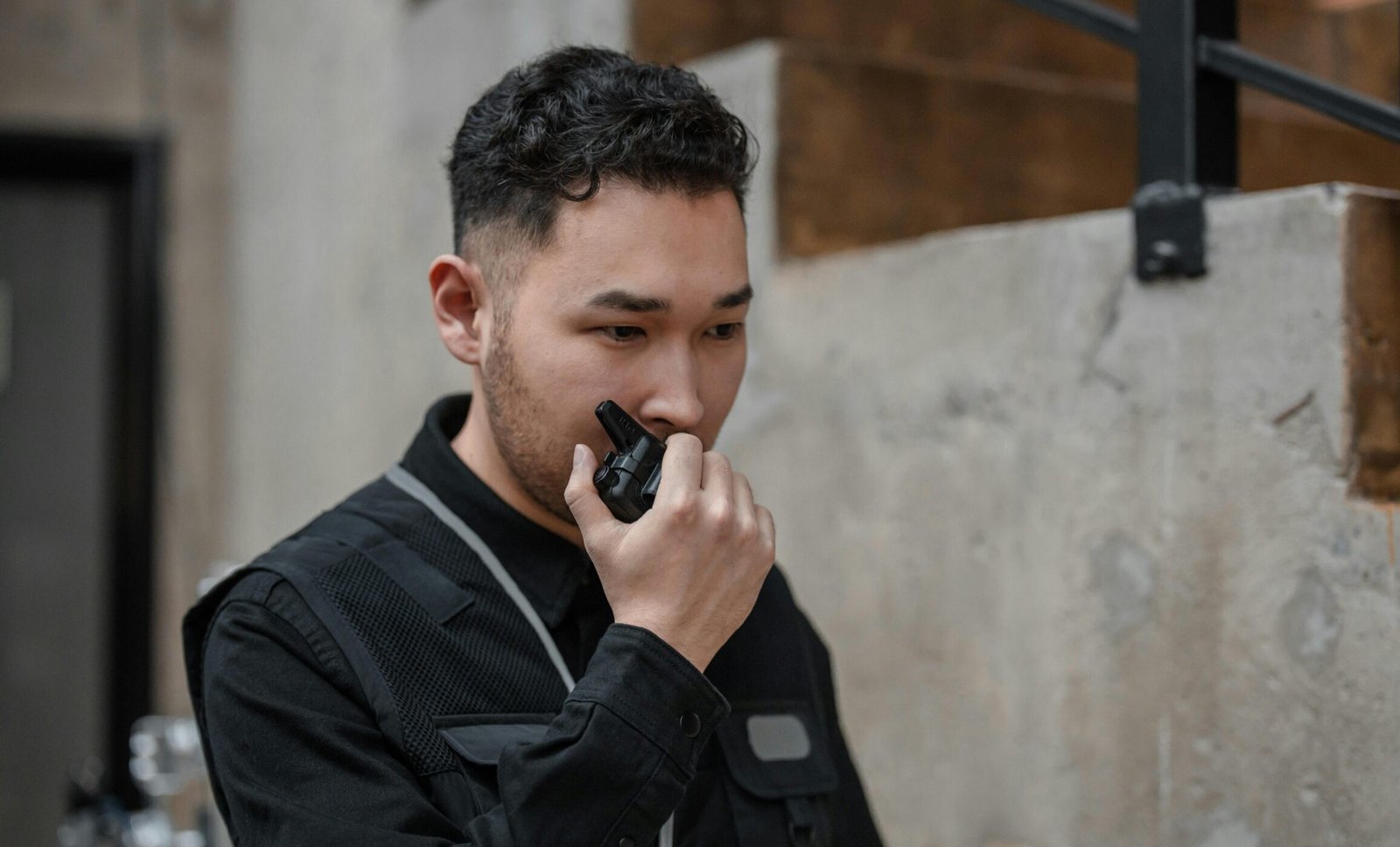 Asian security guard using walkie talkie in an indoor setting, demonstrating communication and alertness.